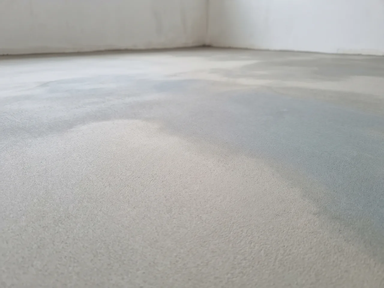 Kale dekvloer die nog droogt in een nieuwbouwwoning, met vers stucwerk op de achtergrond.