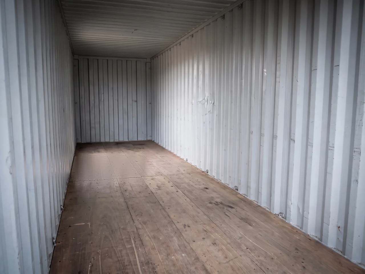 Lege zeecontainer van binnen met golfplaatwanden, plafond en houten vloer tot aan de kopwand.
