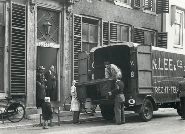 Zwart-witfoto van verhuizers van C.A. van der Lee & Co die een groot eikenhouten meubel in hun verhuiswagen tillen, Minrebroederstraat in Utrecht, 1945 tot 1955. Een ander verhuisbedrijf, niet De Bresser.