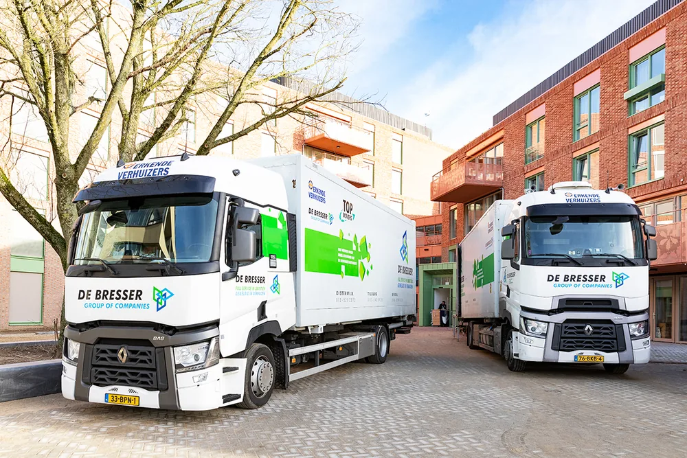 Twee verhuiswagens van De Bresser bij een appartementencomplex
