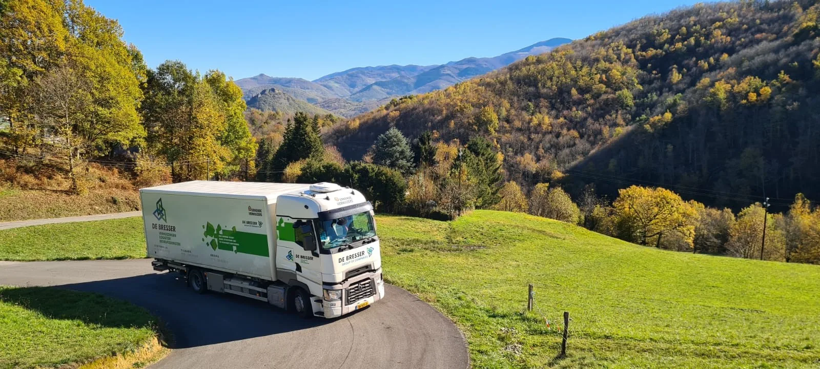 Verhuiswagen van De Bresser op een bergweg in een groen dal in Zwitserland