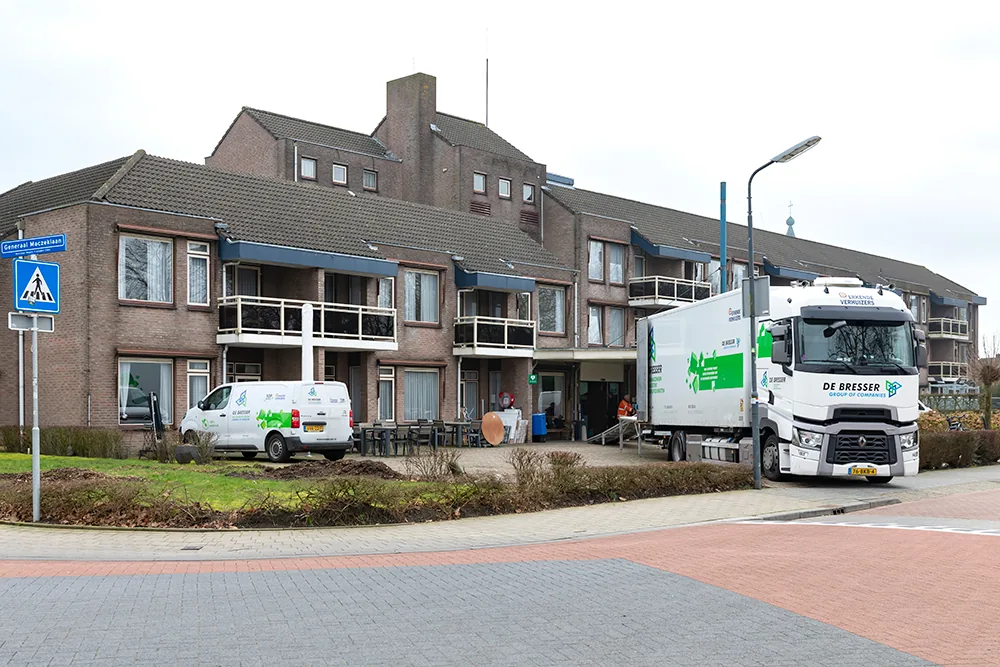 Verhuiswagen en bus van De Bresser bij een zorgcomplex