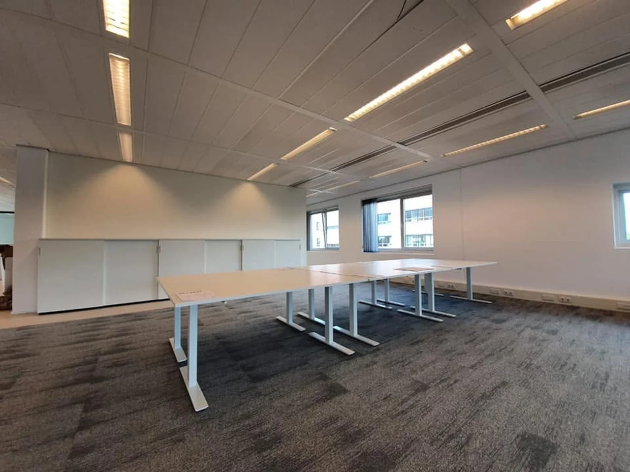 Lege kantoorruimte met lange witte tafels en lage kasten langs de wand