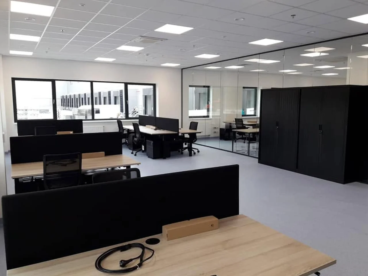 Kantoortuin met bureaus met zwarte scheidingsschermen, bureaustoelen en zwarte kasten