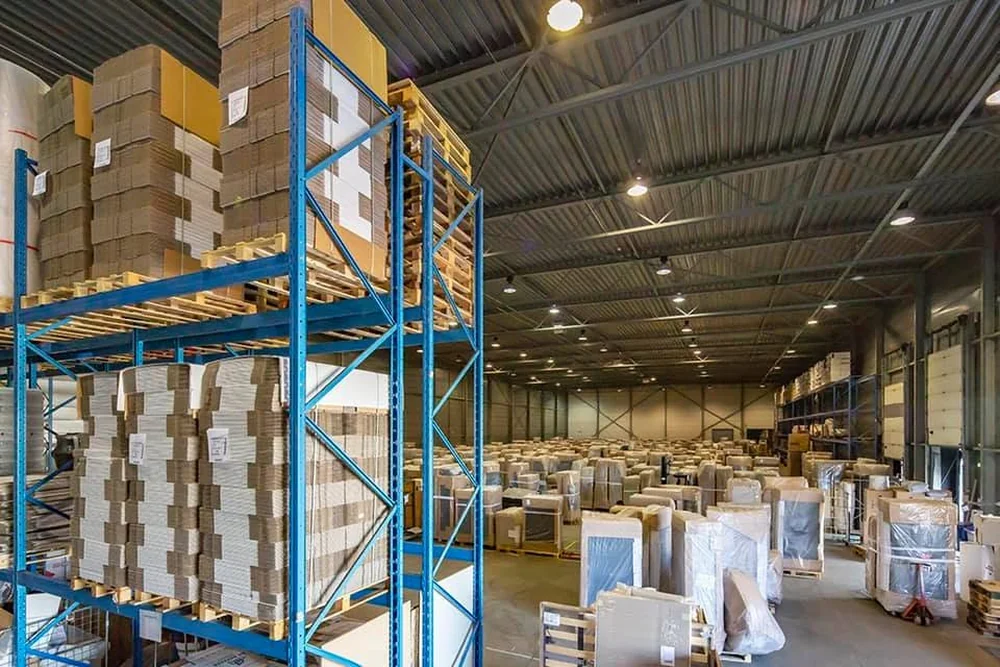 Opslaghal met stellingen vol platte verhuisdozen en in folie verpakt meubilair op pallets