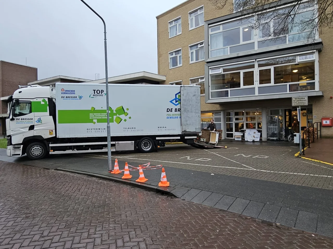 Verhuiswagen van De Bresser voor een kantoorpand, met pionnen op de stoep