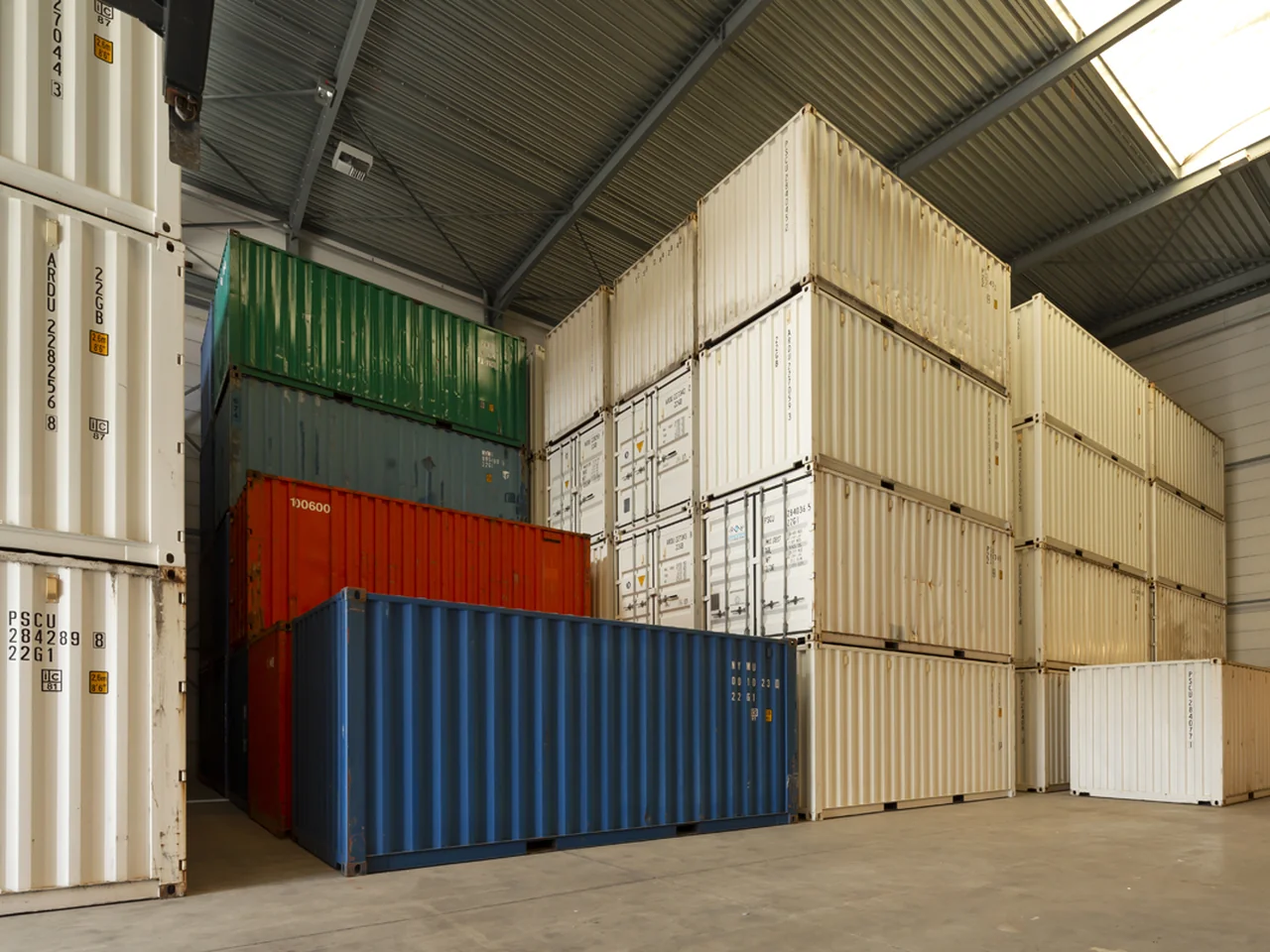 Zeecontainers in verschillende kleuren gestapeld in een opslaghal