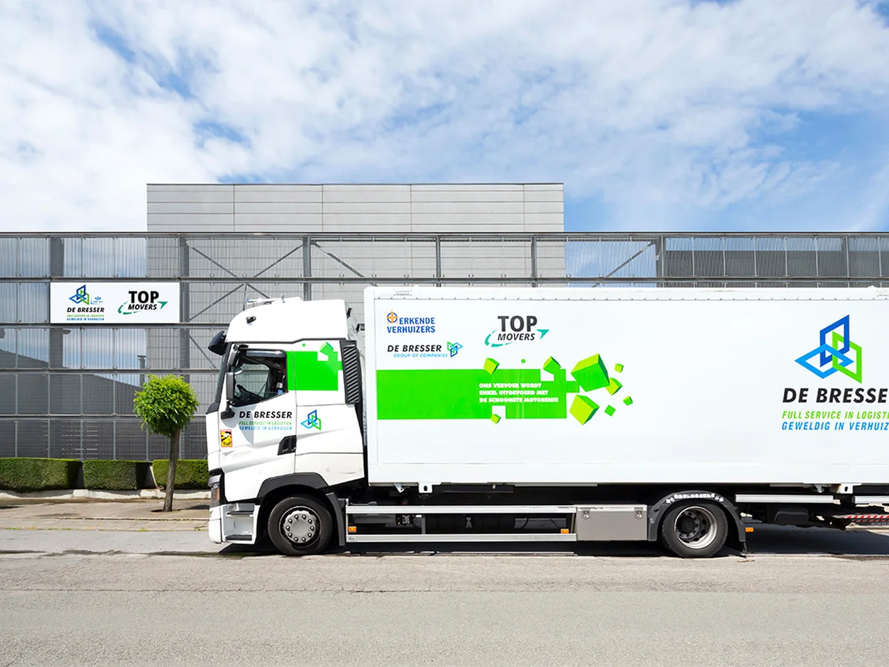Vrachtwagen van De Bresser voor een bedrijfspand met borden van De Bresser en Top Movers