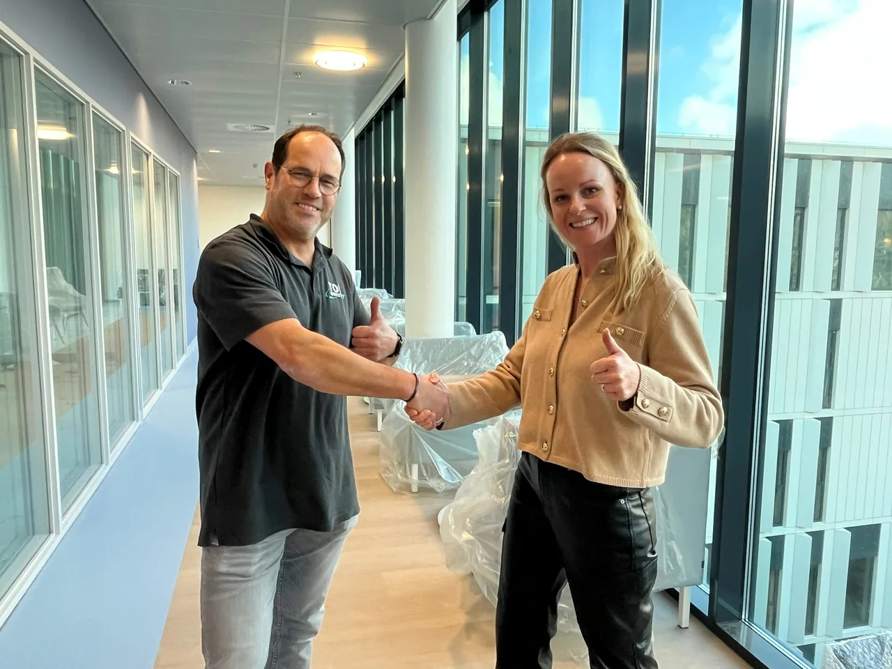 Medewerker in Top Movers-polo geeft een klant een hand in een kantoorgang met ingepakt meubilair