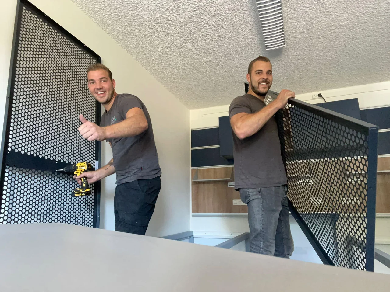 Twee handymannen van De Bresser monteren een metalen hekwerk aan een trapgat