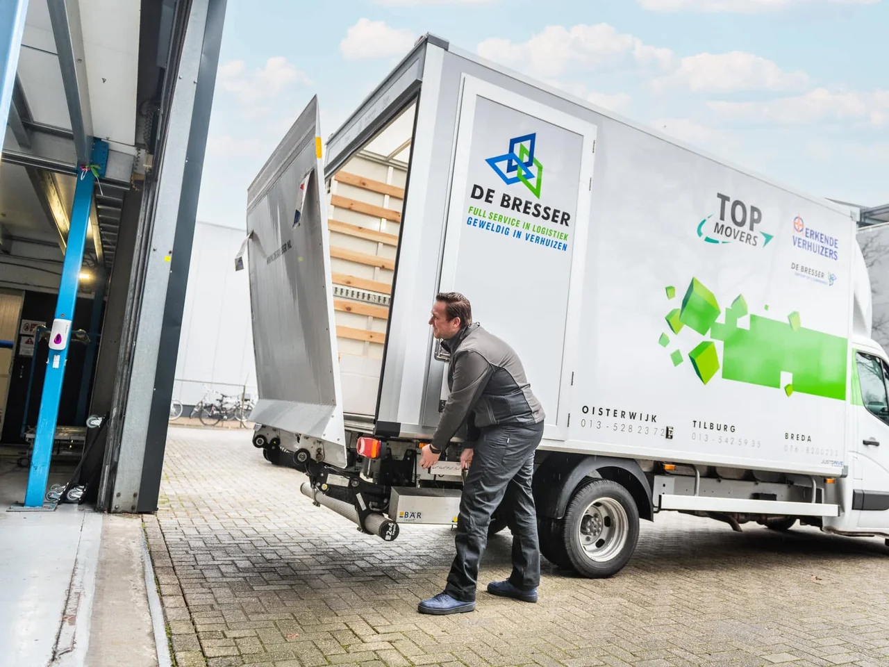Verhuizer van De Bresser bij de laadklep van een eigen bakwagen met open zijdeur