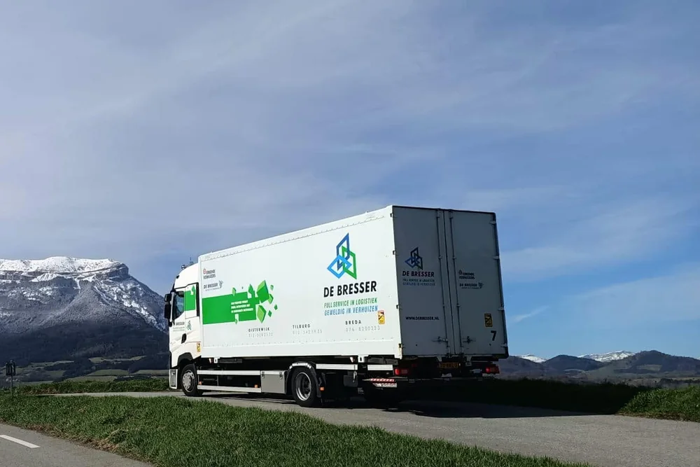 Verhuiswagen van De Bresser op een bergweg met besneeuwde toppen