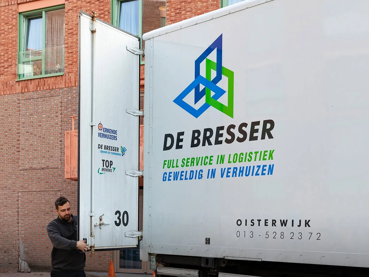 Medewerker van De Bresser opent de achterdeur van een eigen bakwagen met de opdruk full service in logistiek