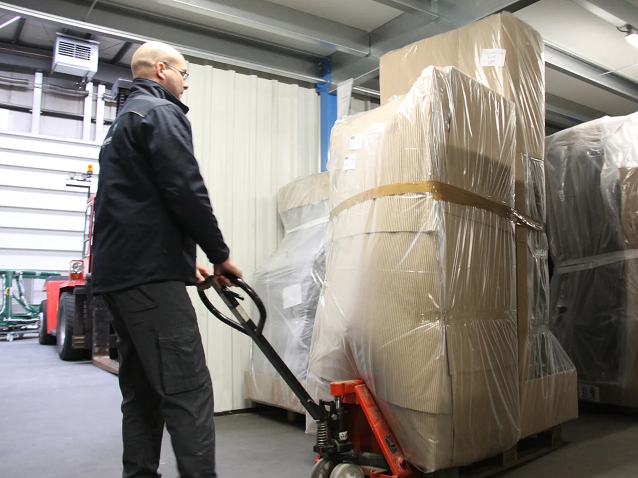 Medewerker van De Bresser trekt met een palletwagen een verpakt meubelstuk door de loods