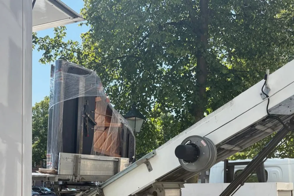 Ingepakte piano op de verhuislift naast de verhuiswagen