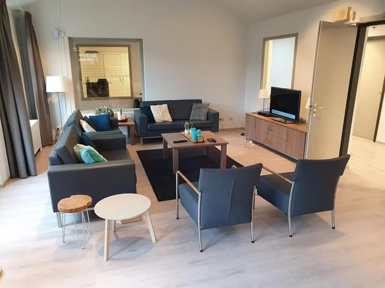 Ingerichte woonkamer met blauwe banken, fauteuils en een televisie