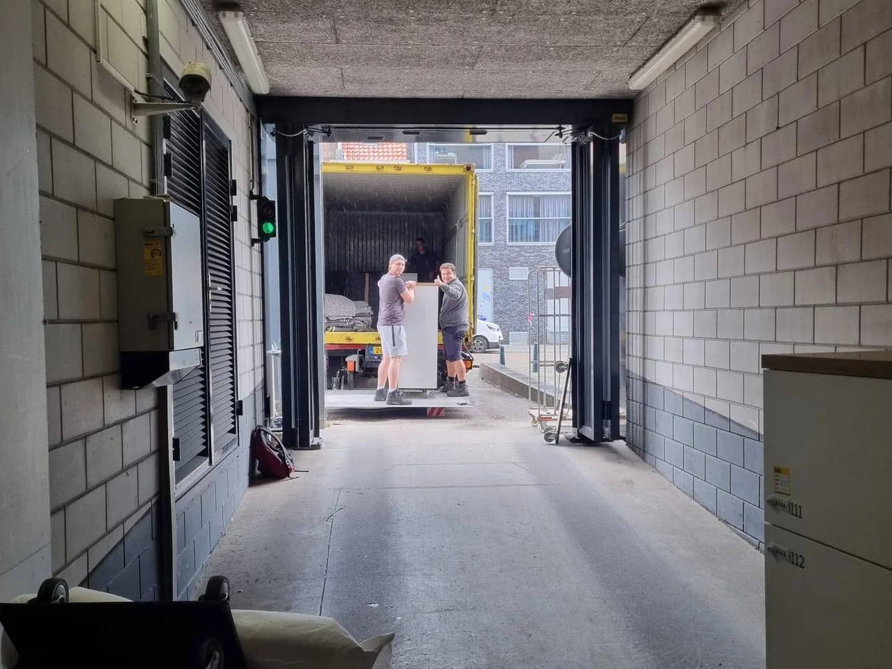Twee verhuizers van De Bresser rijden een kast door een laadgang naar de verhuiswagen