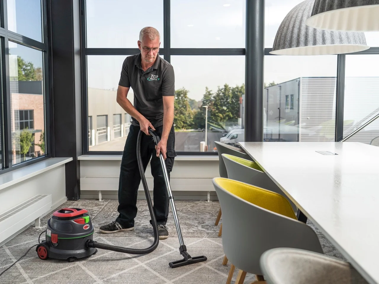 Medewerker in Top Movers-polo zuigt de vloer van een kantoor na de verhuizing
