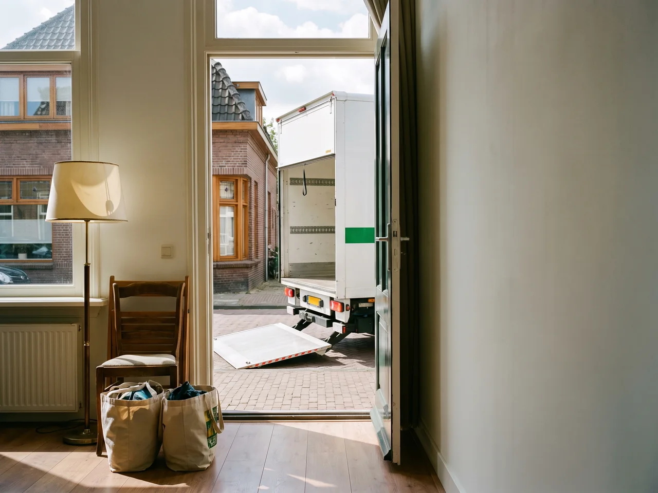 Tassen en een stoel staan apart bij de voordeur, buiten wacht de verhuiswagen met de klep omlaag