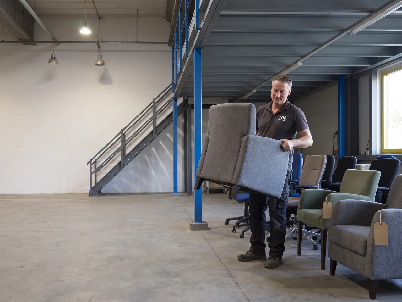 Medewerker van De Bresser zet een gebruikte fauteuil bij een rij stoelen voor hergebruik in de opslaghal