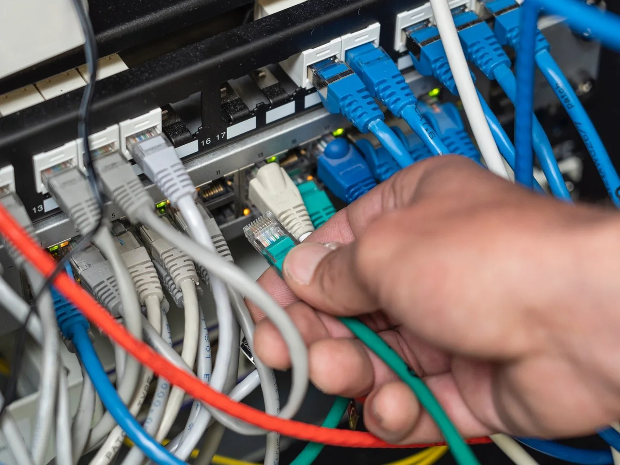 Hand steekt netwerkkabels in een patchpaneel