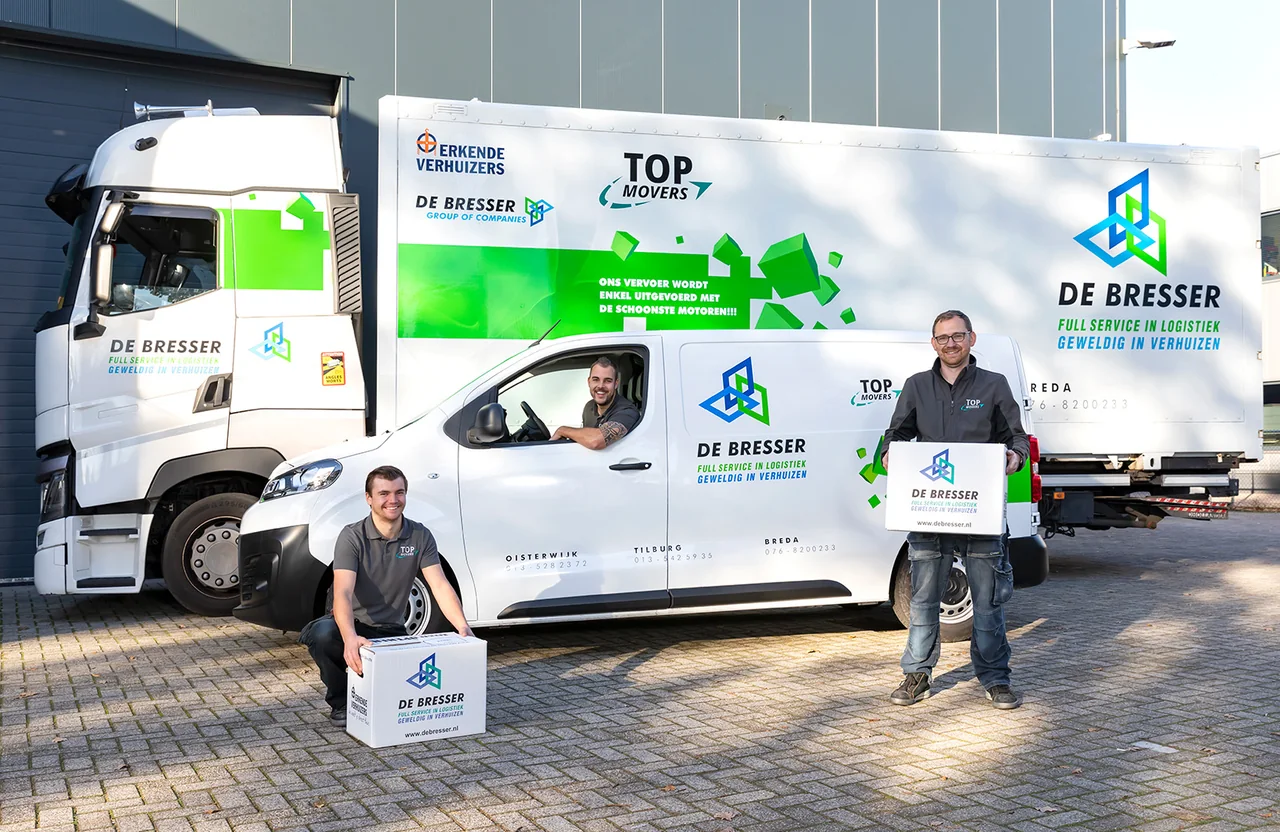 Drie medewerkers met verhuisdozen van De Bresser bij een vrachtwagen en een bestelbus van De Bresser