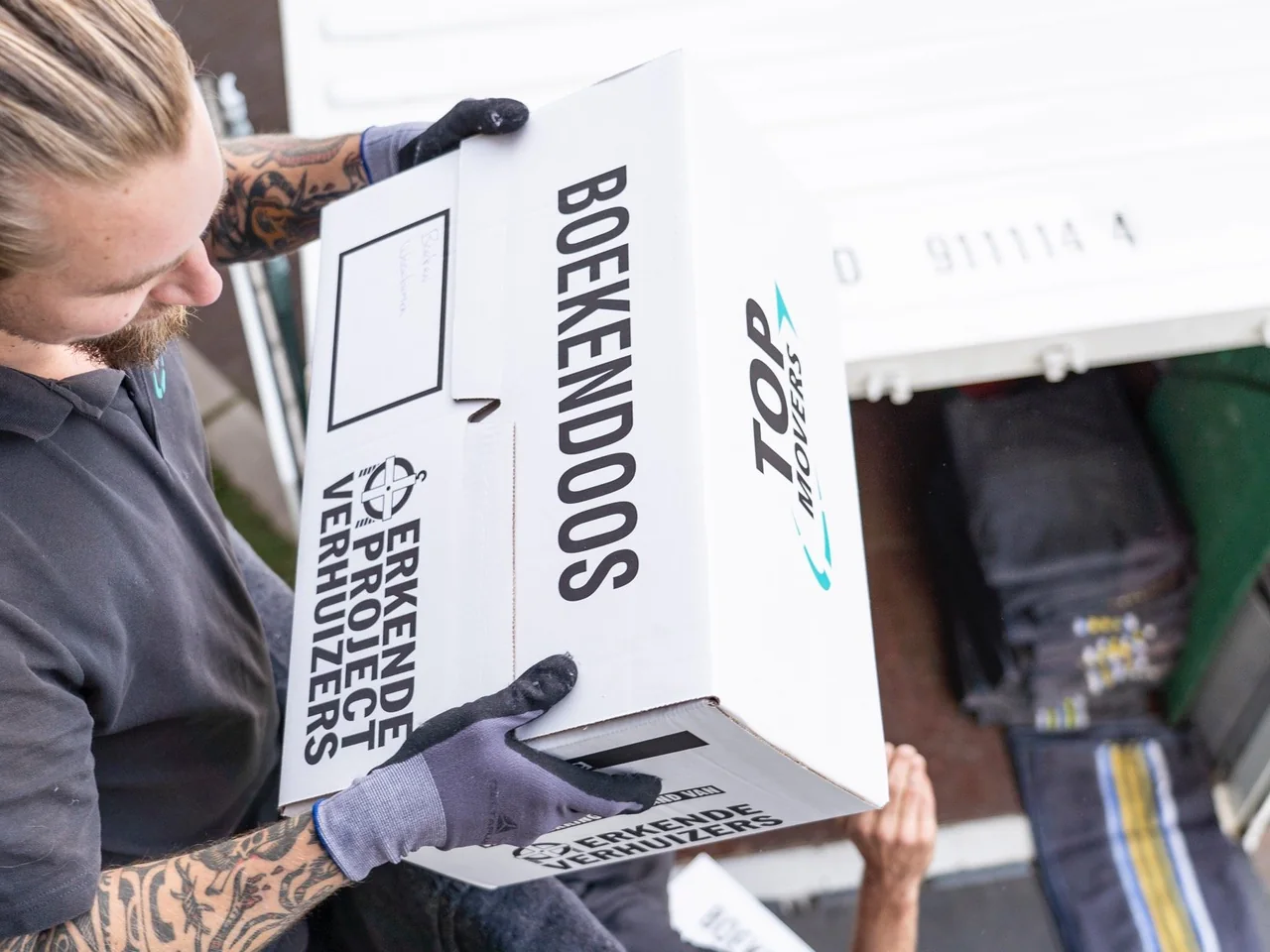 Verhuizer tilt een boekendoos van Top Movers met het keurmerk Erkende Projectverhuizers uit de wagen, van boven gezien