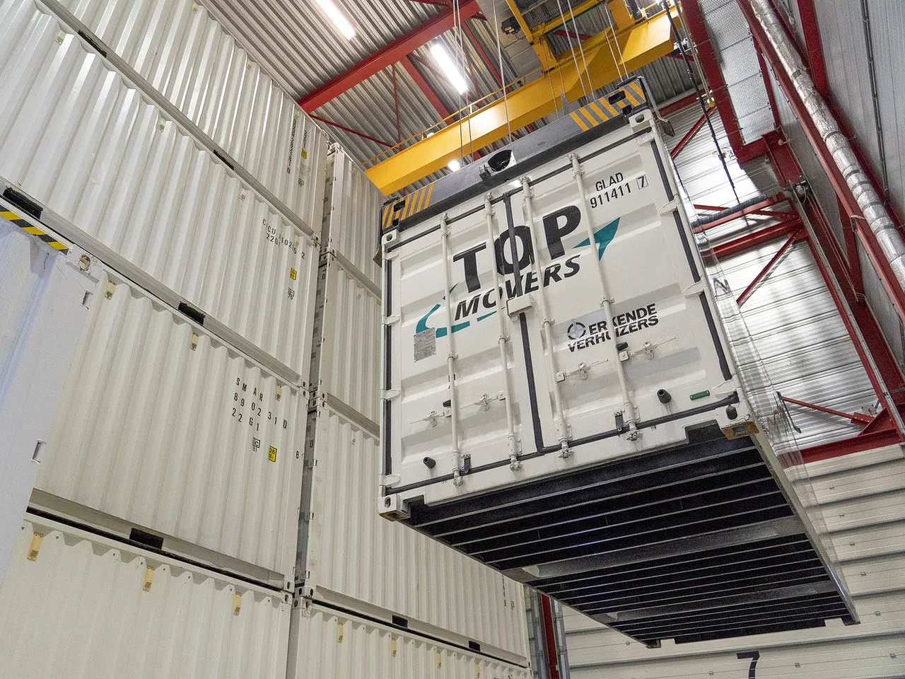 Opslagcontainer van Top Movers hangt aan de loopkraan tussen gestapelde containers in de opslaghal
