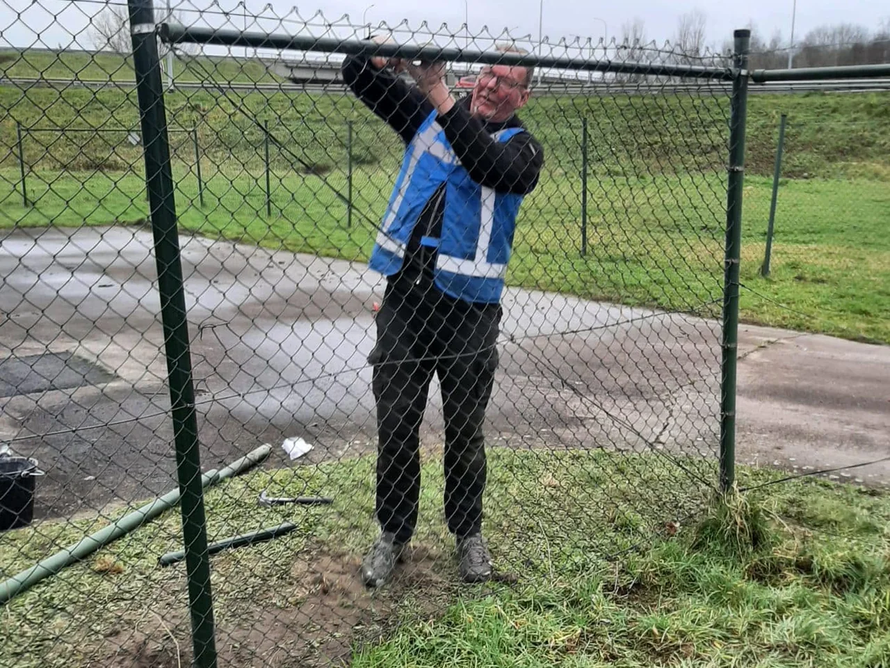 Handyman van De Bresser zet een hekwerk vast langs een terrein