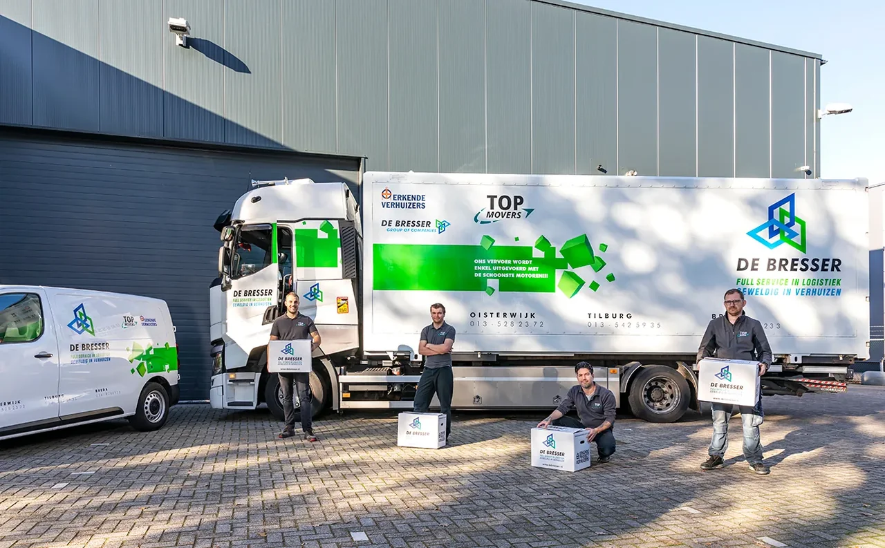Vier medewerkers met verhuisdozen voor een vrachtwagen en een bestelbus van De Bresser bij een loods