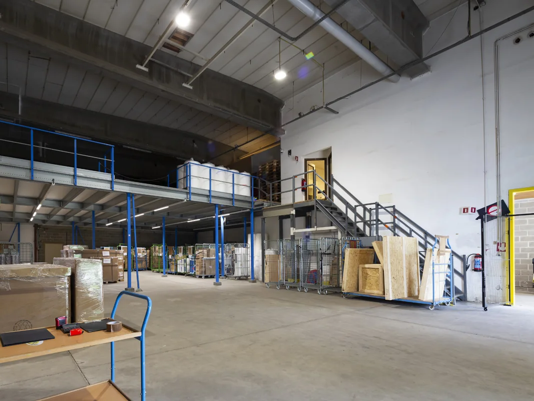 Magazijn van De Bresser met entresol, rolcontainers, dozen op pallets en een trap naar de verdieping