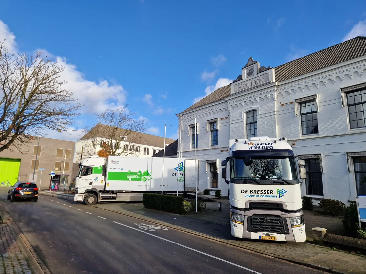 Twee verhuiswagens van De Bresser in een straat voor een wit pand