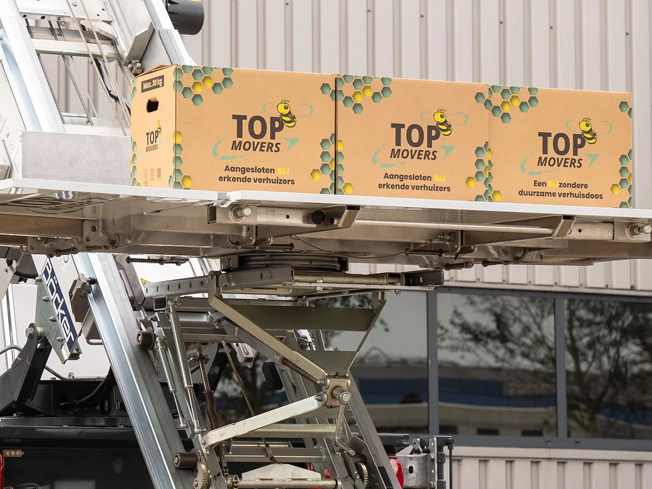 Ladderlift met drie verhuisdozen van Top Movers op het plateau voor een bedrijfshal
