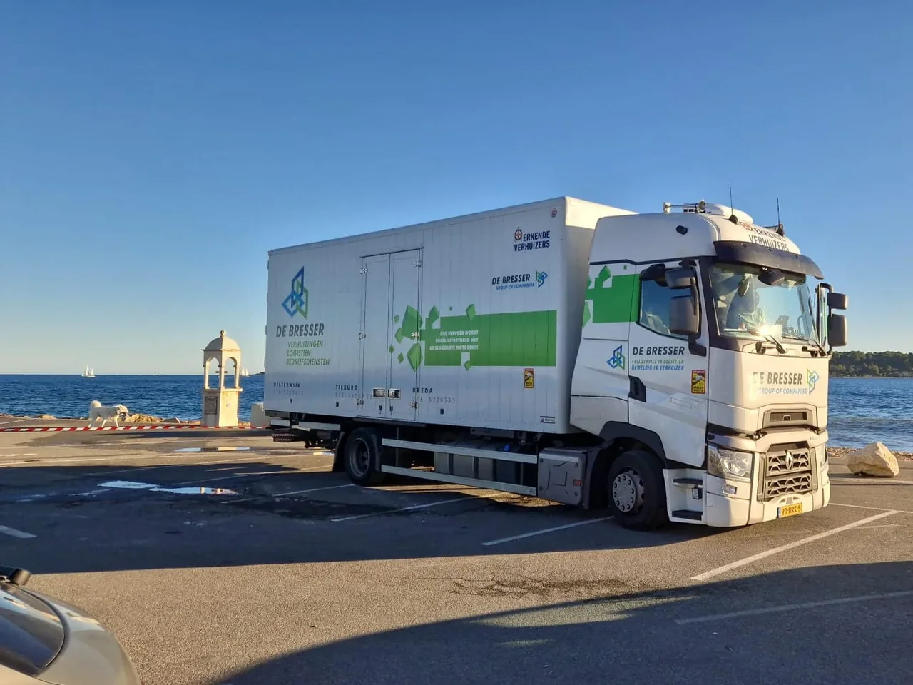 Vrachtwagen van De Bresser op een parkeerplaats aan zee, met zeilboten in de verte