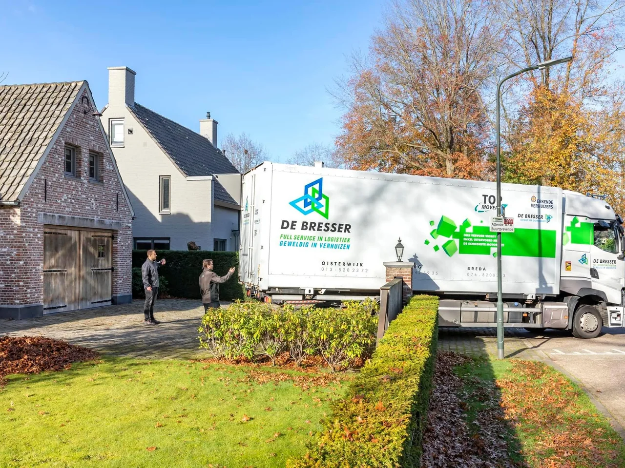 Verhuiswagen van De Bresser bij een villa in de herfst, met twee verhuizers op de oprit