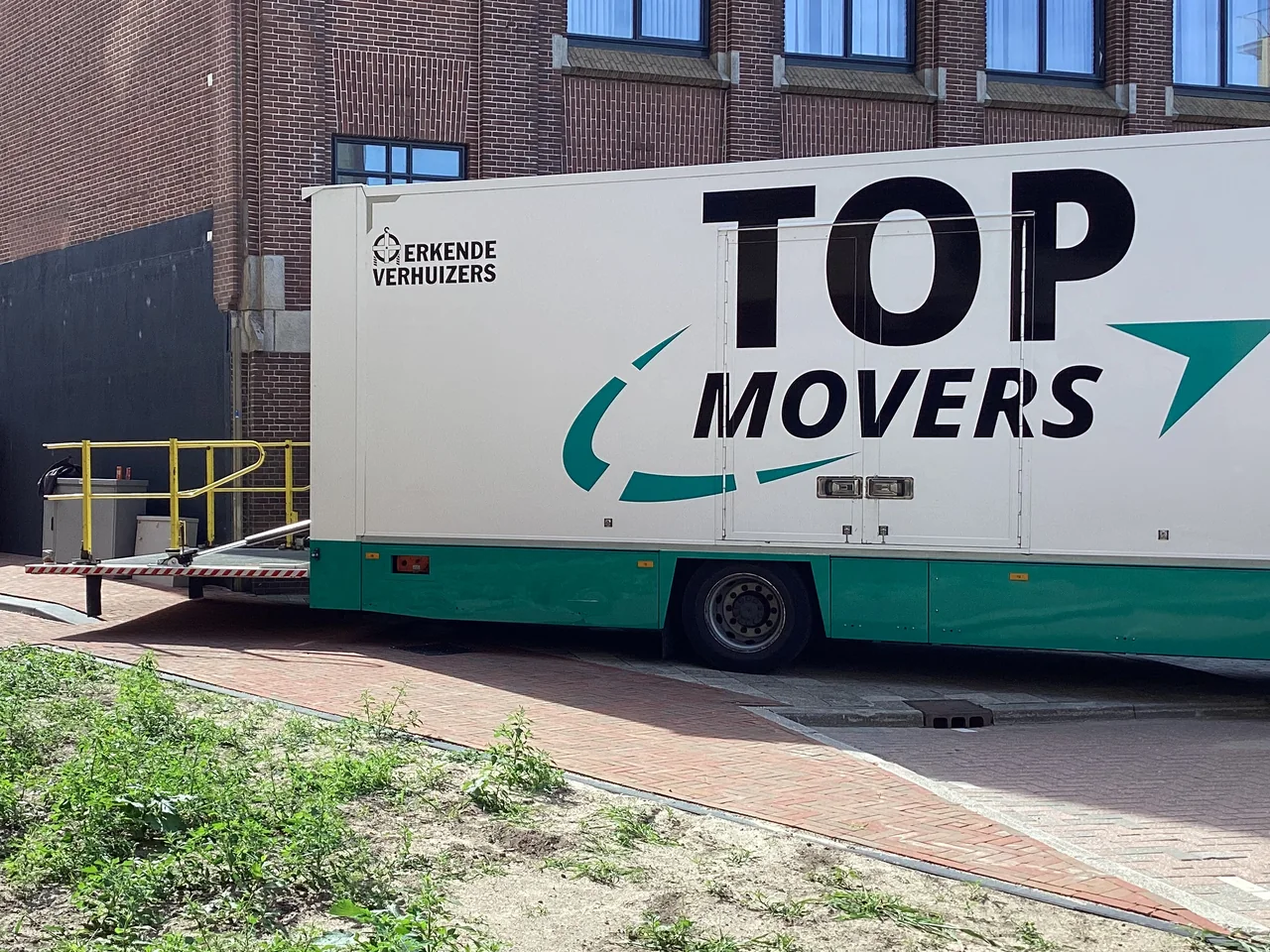Verhuiswagen van Top Movers met de laadklep omlaag bij een bedrijfspand