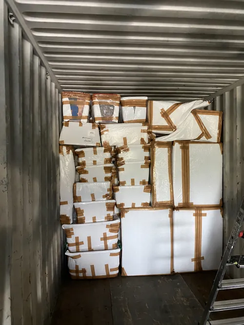 Container met gestapelde, wit ingepakte meubels en pakketten