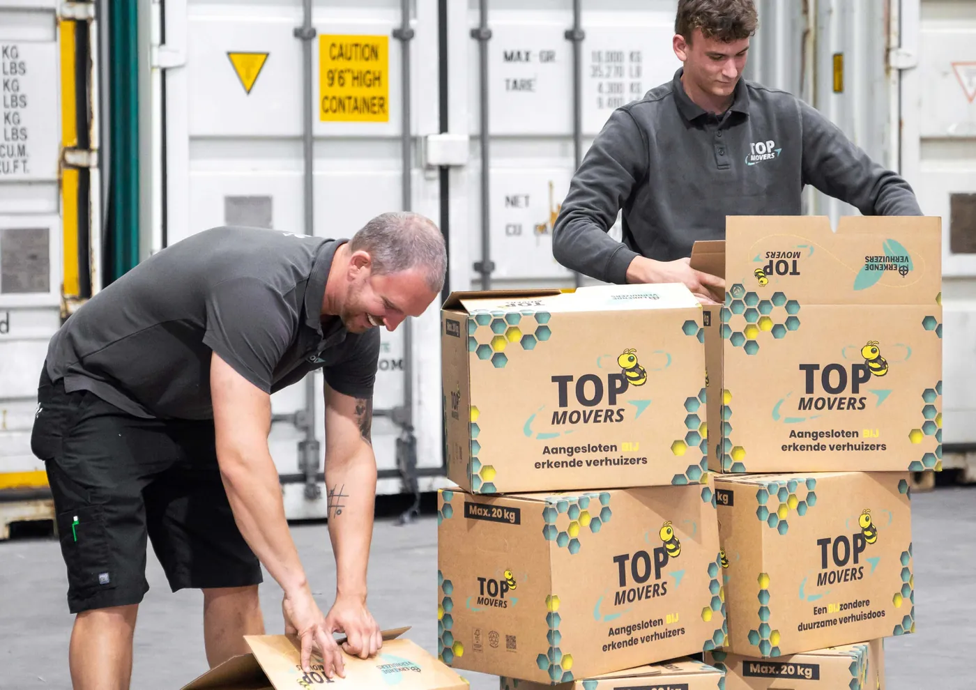 Twee verhuizers pakken verhuisdozen van Top Movers in voor een rij containers