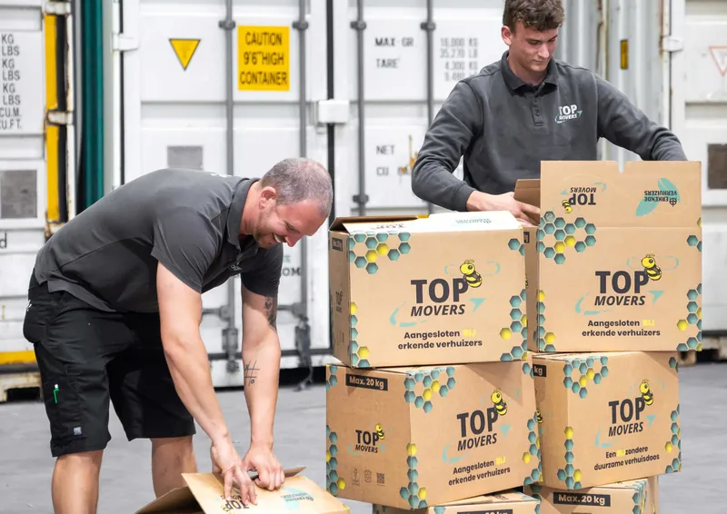 Twee verhuizers pakken verhuisdozen van Top Movers in voor een rij containers